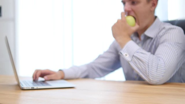 Young businessman is biting apple in the office. Blurred background. Focus is on apple. Close up. Copy space. 4K.