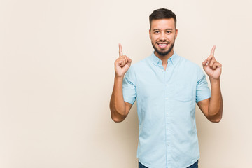 Young south-asian man indicates with both fore fingers up showing a blank space.