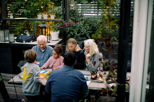 High angle view of family playing board game on table while sitting in patio
