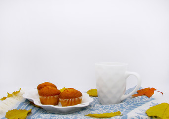 white Cup of tea and cupcake  on blue tea towel and autumn leaves