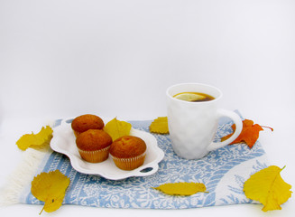 white cup of black tea with lemon, cupcake  on blue tea towel and autumn leaves