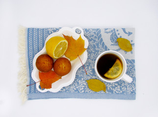 white сup of black tea with lemon, cupcake  on blue tea towel and autumn leaves