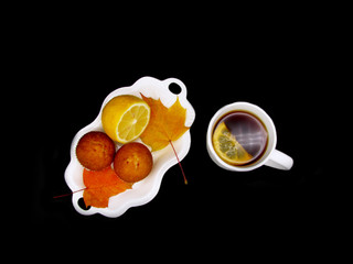 сup of tea with lemon, cupcake, autumn leaves  on dark background