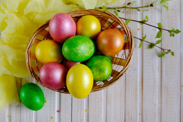Basket with painted Easter eggs and birch branches with leaves on a wooden white table