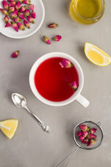 Herbal tea with pink roses in the white cup  on the grey concrete background. Top view. Location vertical. Copy space.