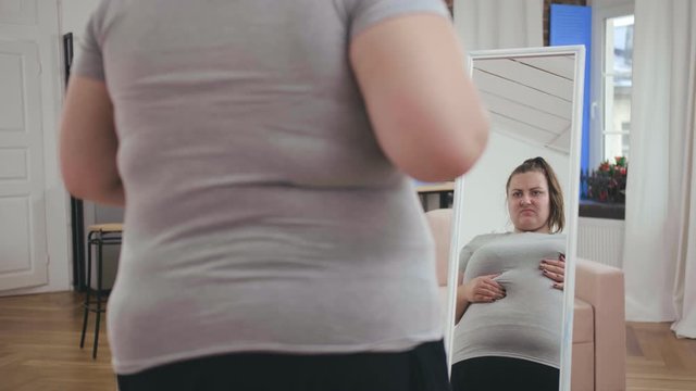 Overweight girl checking skin in front of mirror, looking at cellulite on body