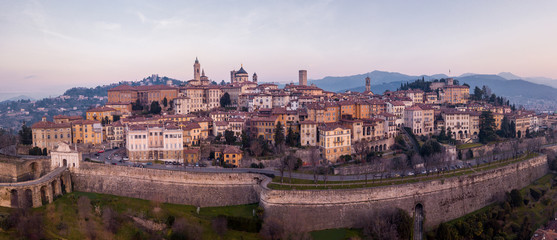 Bergamo, Italy. Drone aerial view of the old town during sunrise. Landscape at the city center, its historical buildings and the Venetian walls a Unesco world heritage - obrazy, fototapety, plakaty