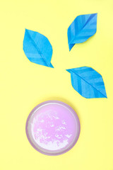 glass bowl filled with a purple liquid soap. on a yellow background are blue petals.