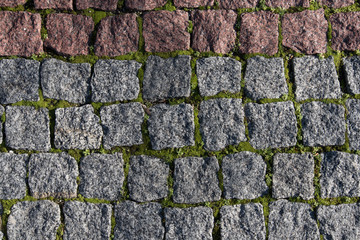 Paving stones made of natural stone. Paths for pedestrians. Beautiful square-shaped stones. Grass breaks through the rocks. The view from the top.