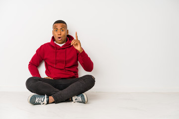 Young latin man sitting on the floor isolated having an idea, inspiration concept.