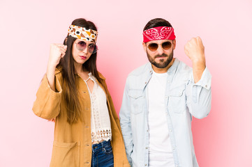 Young caucasian couple wearing a music festival clothes isolated showing fist to camera, aggressive facial expression.