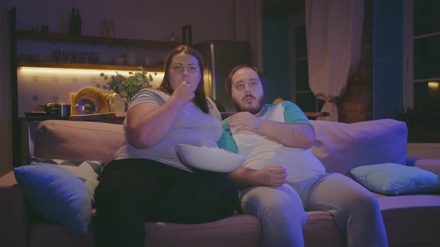 Man and woman watching tv and eating popcorn at home in evening