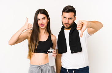Young caucasian fitness couple isolated showing thumbs up and thumbs down, difficult choose concept