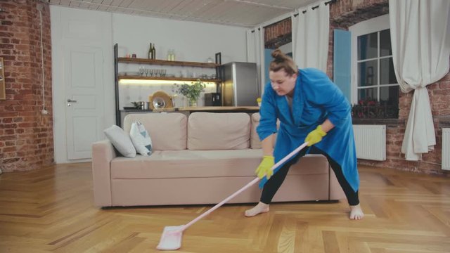 Overweight woman cleaning floor in living room with wet mop