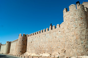 The defensive walls at the Spanish medieval city of Avila. Defensive battlements set against a blue summer sky in the heart of Spain / copy space.