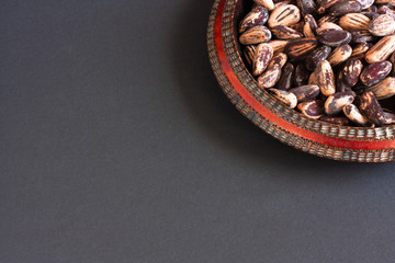 Pine nuts on wooden plate with red border on black background.