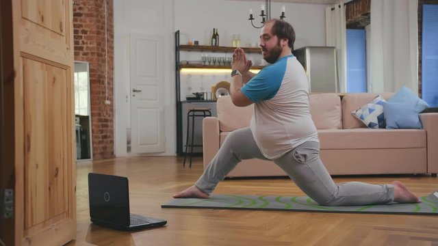 Funny obese man doing fitness exercises with video on laptop at home