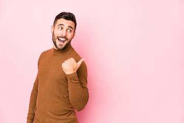 Young caucasian man against a pink background isolated points with thumb finger away, laughing and carefree.