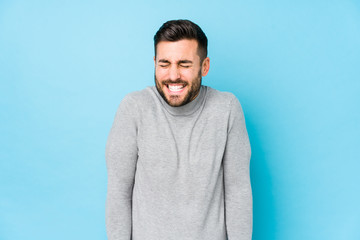 Young caucasian man against a blue background isolated laughs and closes eyes, feels relaxed and...