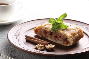 Concept of German cuisine. Apple strudel with cinnamon and nuts with a cup of tea on a light background. Background image, copy space