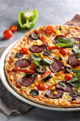 The concept of Italian cuisine. Pepperoni pizza with tomatoes, basil, corn and olives on a light background. Background image, copy space