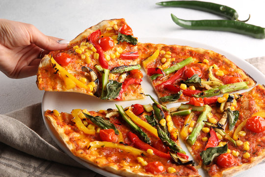 The concept of Italian cuisine. Vegetable pizza with tomatoes, peppers, corn and asparagus on a light background with hand. Background image, copy space