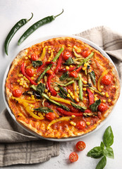 The concept of Italian cuisine. Vegetable pizza with tomatoes, peppers, corn and asparagus on a light background. Background image, copy space