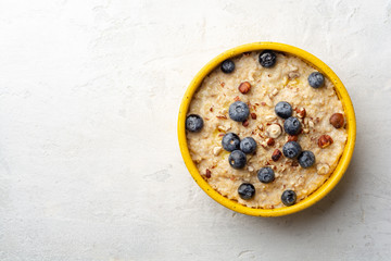 Oatmeal porridge with hazelnuts and blueberries in bowl on concrete background. Top view, copy space.