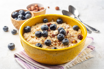 Oatmeal porridge with hazelnuts and blueberries in bowl on concrete background. Selective focus.