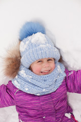 Little cheerful girl lies in the snow