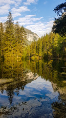 Reflection of the mountain landscape in a calm surface of Green Lake, Austria. The reflection is in the shade. High mountains are surrounded by dense forest. Spring in Alpine valley. Mirroring effect