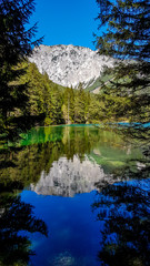 Fototapeta na wymiar Reflection of the mountain landscape in a calm surface of Green Lake, Austria. The reflection is in the shade. High mountains are surrounded by dense forest. Spring in Alpine valley. Mirroring effect