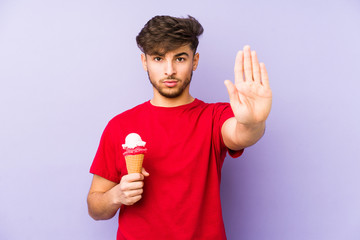 Young arabian man holding a ice cream standing with outstretched hand showing stop sign, preventing you.