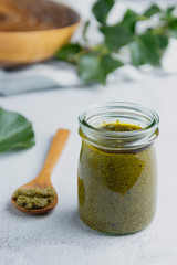 Glass jar with pesto sauce on white textured background table close up. Pasta sauce.