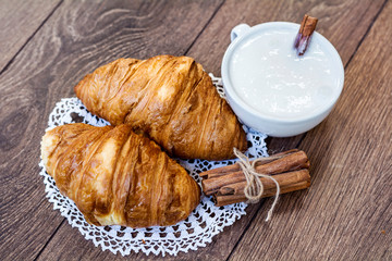 Cup of  Milk, Fresh Baked Croissants and Cinnamon Sticks for Breakfast on a Wooden Background