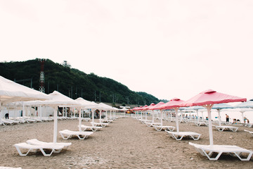 white sunbeds with colorful umbrellas on a pebble beach in the summer