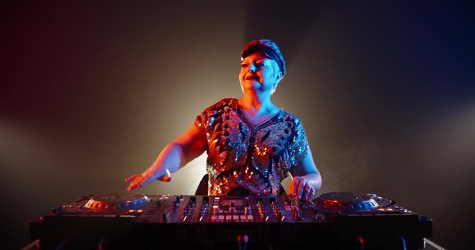 Authentic grandma DJ with shiny clothes and makeup performing in a nightclub with neon lights 4k footage