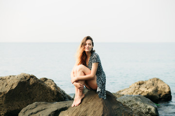 a young beautiful girl in a dress on large stones, a picturesque place on the sea coast