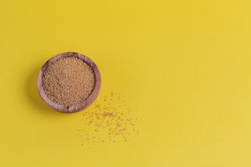 Brown sugar heap in bowl on yellow background