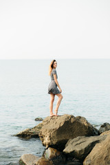 a young beautiful girl in a dress on large stones, a picturesque place on the sea coast