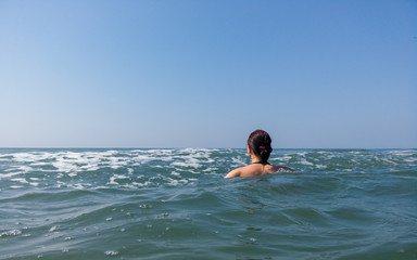 Young woman in black swimsuit spends time in sea. Adult lady swims towards the waves.