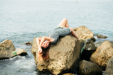 a young beautiful girl in a dress on large stones, a picturesque place on the sea coast