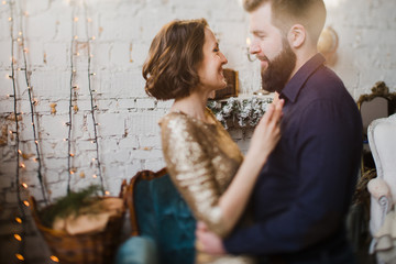 Celebrating Christmas together. Young caucasian couple in holiday clothes hugging near the Christmas tree. New Year, Valentine, love, romance concept.