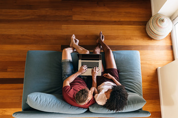 Multiethnic lovers sitting on couch with laptop together