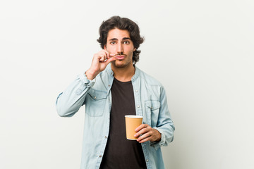 Young cool man drinking a coffee with fingers on lips keeping a secret.
