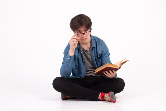 Portrait of young man in eyeglasses drinking coffee and looking at open book isolated on a white background.