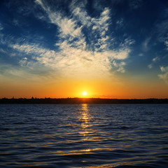 low orange sunrise over dark water in river