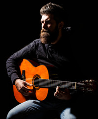 Bearded man playing guitar, holding an acoustic guitar in his hands. Bearded guitarist plays. Play the guitar. Beard hipster man sitting in a pub. Live music