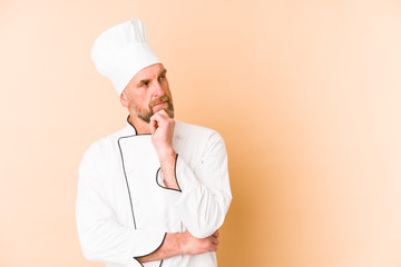 Chef man isolated on beige background looking sideways with doubtful and skeptical expression.