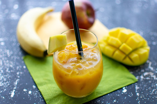 leckerer Mango Smoothie mit crushed ice und Strohhalm im Trinkglas. Im Hintergrund liegen frische Früchte